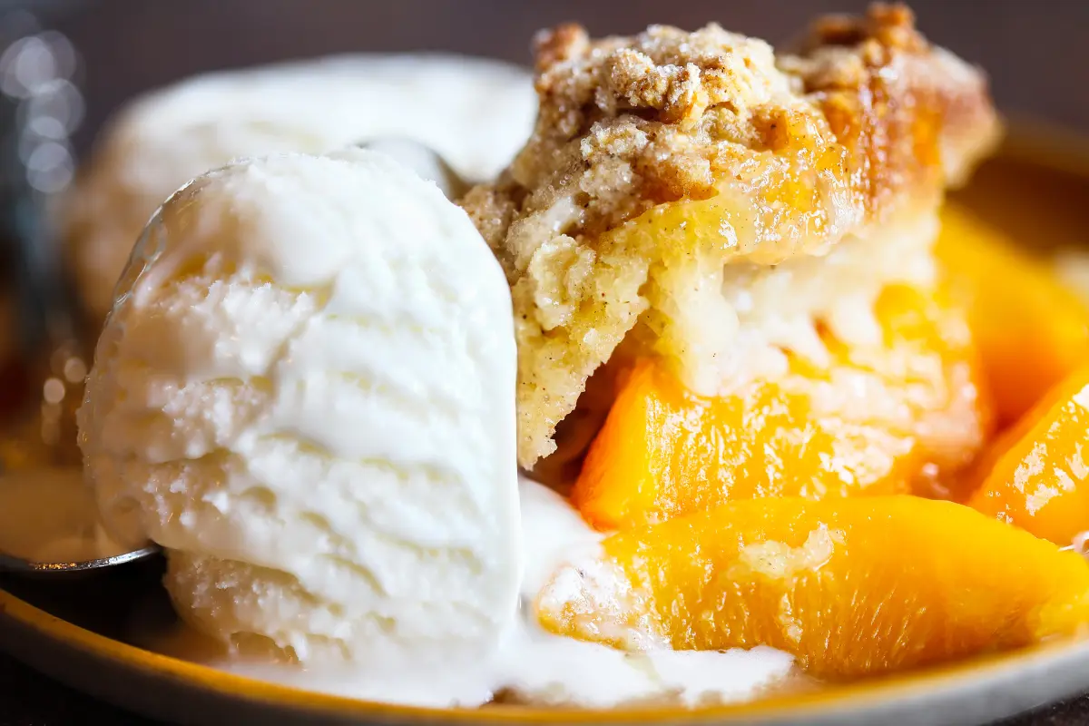 Golden peach cobbler with a crispy topping and melting vanilla ice cream on the side.